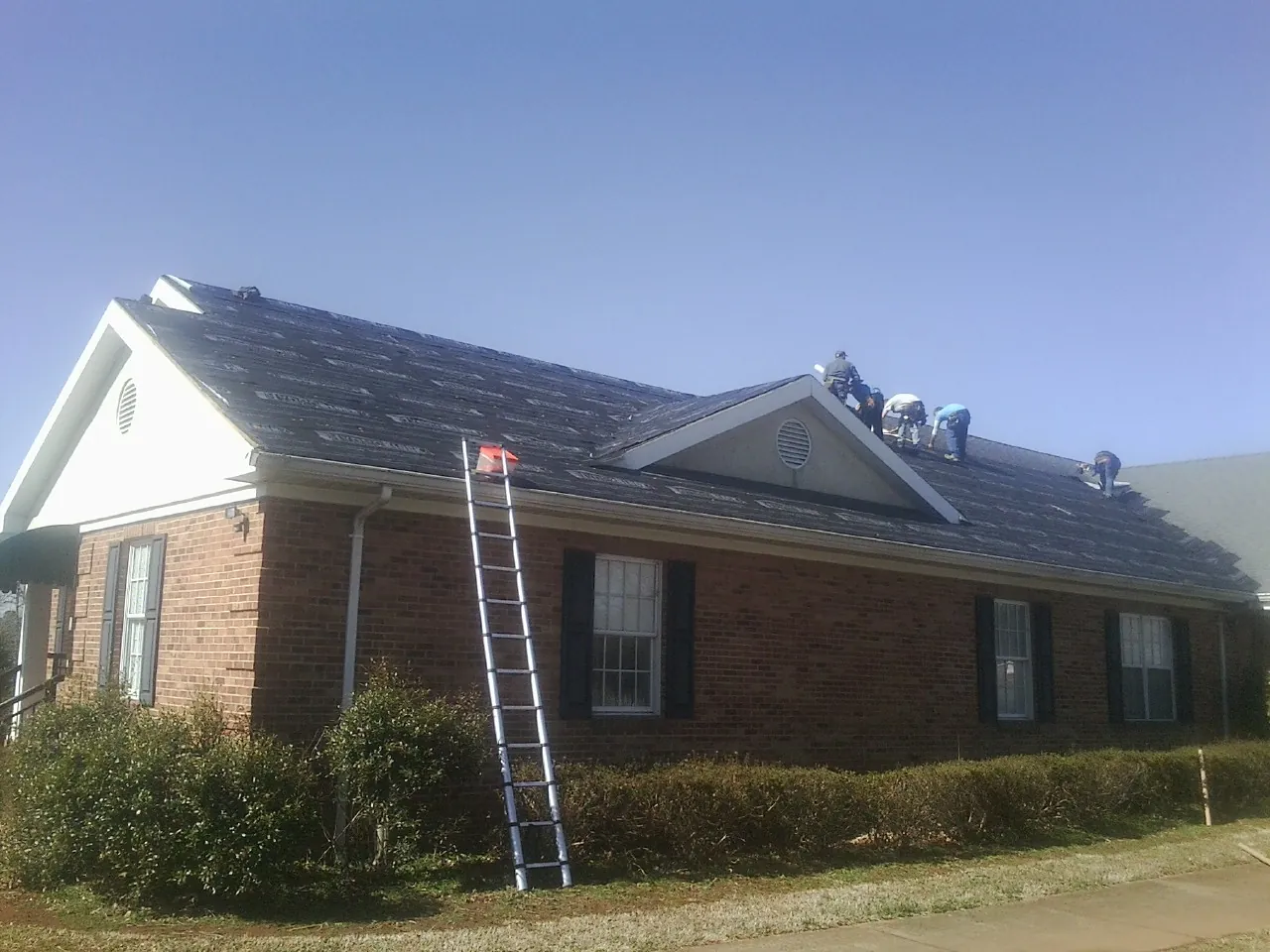 Crew tearing shingles off a brick ranch roof with a ladder set — Emergency Roof Repair work by our crew in West Jordan
