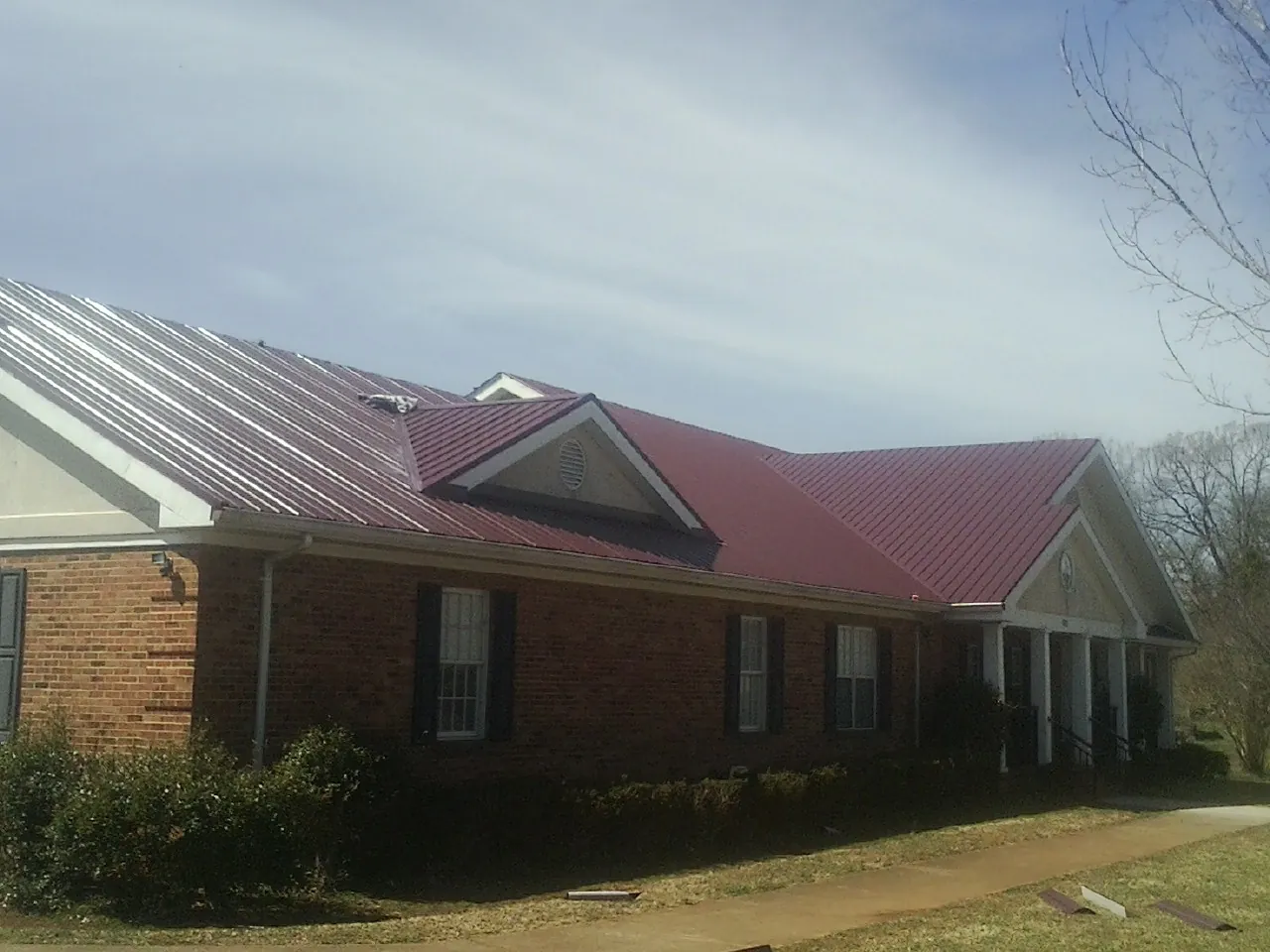 Red metal roof with gabled entries on a long brick building, from a Hail Damage Roof Repair job in West Jordan