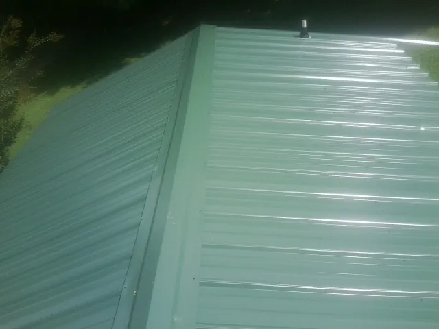 New green metal panels meeting at the ridge of a roof — Flat Roof Repair work by our crew in West Jordan