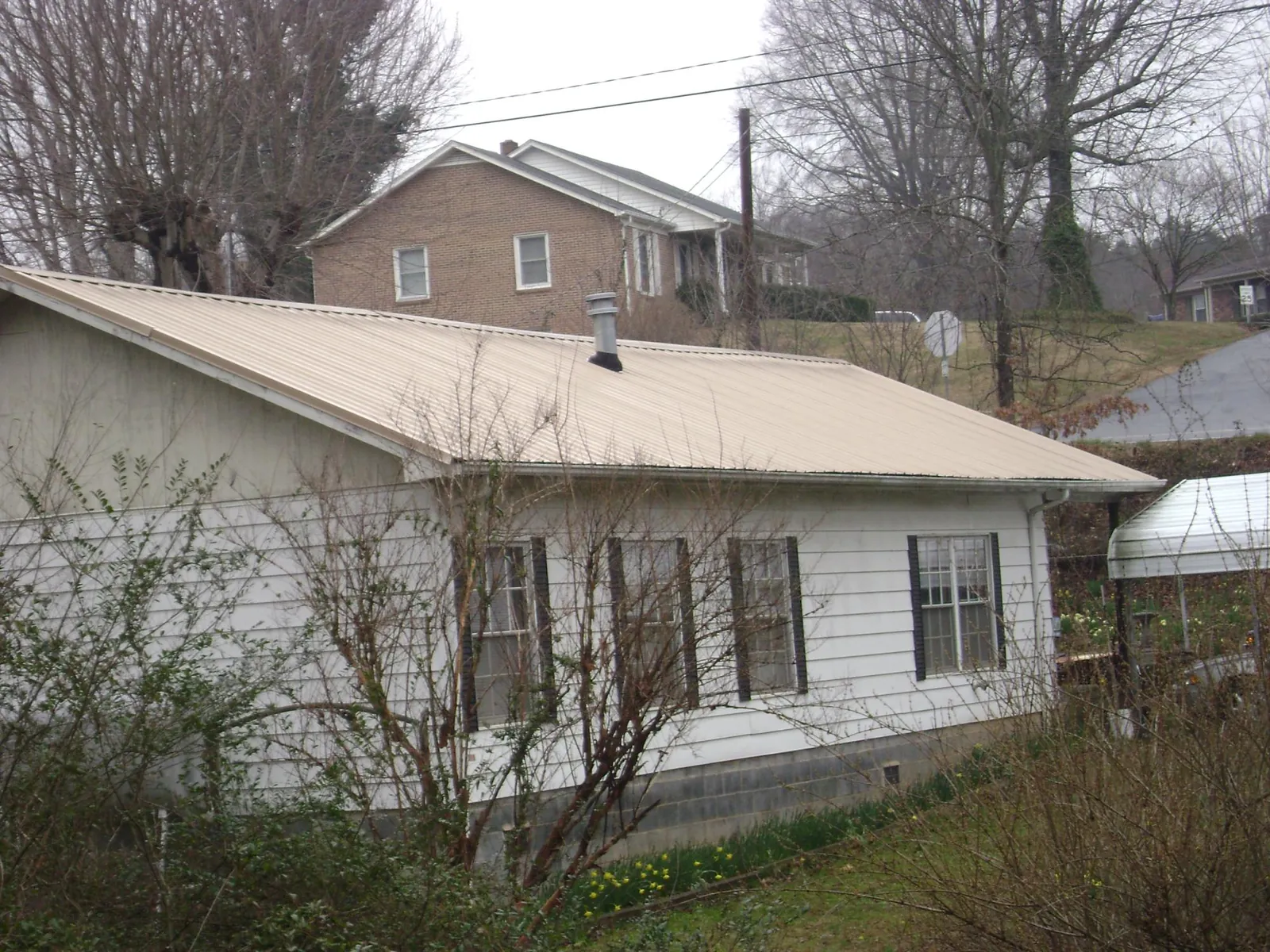 Tan metal roof on a white sided house set into a hillside — Commercial Roofing by Roofing Brothers in West Jordan